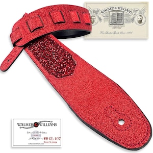 May include: A red glitter guitar strap with black backing and accents. The strap features a padded shoulder section and a tail with a buttonhole. The Walker & Williams logo and product information are visible on a card.