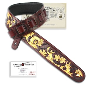 Peut inclure: Une sangle de guitare en cuir marron avec des motifs floraux dorés en relief. La sangle est dotée d'une section rembourrée pour plus de confort et est réglable. La sangle est étiquetée "LHR-27 Gold Waves" et "Walker & Williams Established in 1894".