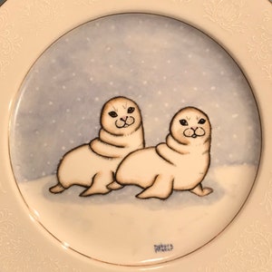 Two baby white seals on a round 10 inch plate with white design on edges.