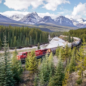 May include: A red train with the words "Canadian Pacific" on the side travels through a snowy mountain valley. The train is surrounded by evergreen trees and snow-capped mountains.