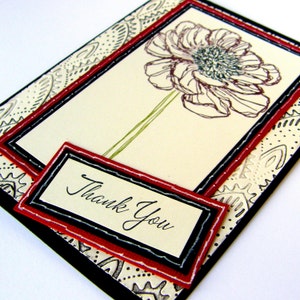May include: A white card with a black and red border. The card has a simple line drawing of a flower and the words "Thank You" written in black.
