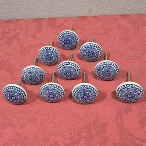 May include: Ten white ceramic cabinet knobs with blue and white floral designs. The knobs have a silver screw in the center.