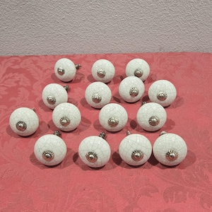 May include: A collection of 15 white ceramic cabinet knobs with a crackled finish and silver accents.