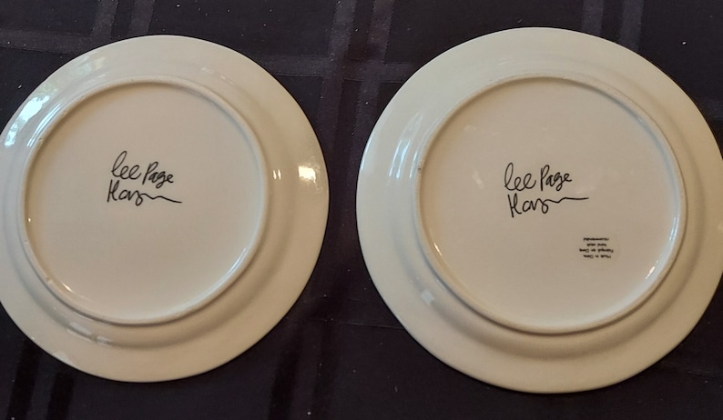 May include: Two white ceramic plates with a black handwritten signature that reads "Lee Page Kars".