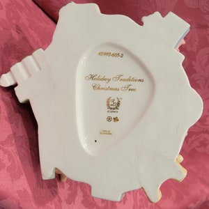 Op de afbeelding: Witte porseleinen kerstboomversiering met gouden opschrift "Holiday Traditions Christmas Tree" en het Lenox-logo. De versiering heeft productnummer 45997-605-2.