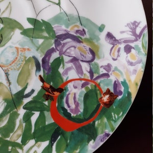 Puede incluir: Un plato de cer&aacute;mica blanco con un dise&ntilde;o floral con acentos morados, verdes y naranjas. Un peque&ntilde;o p&aacute;jaro est&aacute; posado en una rama con un c&iacute;rculo rojo alrededor.