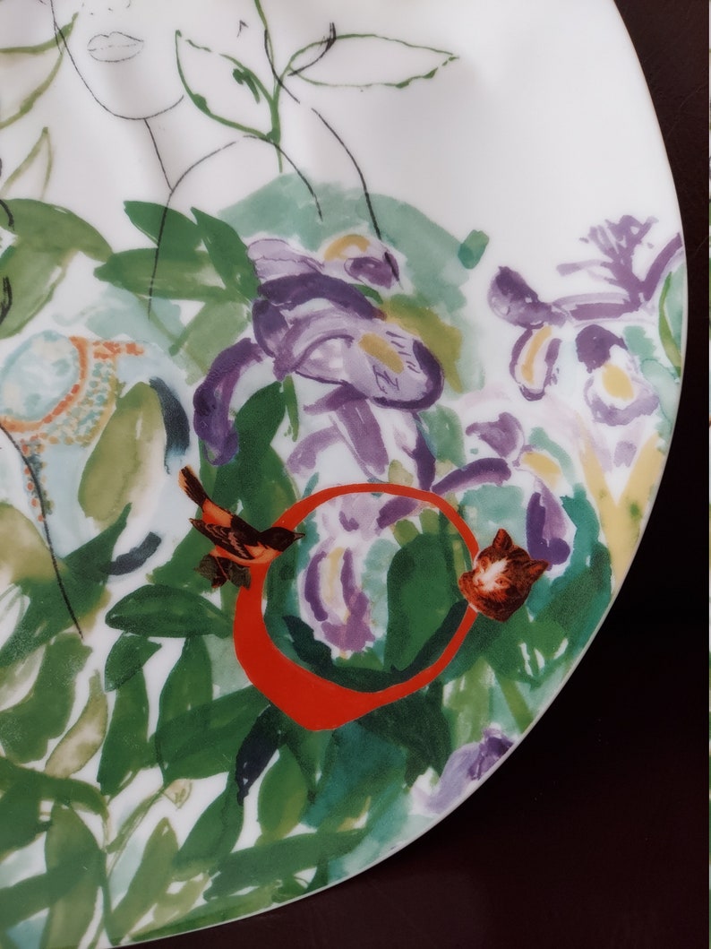Puede incluir: Un plato de cer&aacute;mica blanco con un dise&ntilde;o floral con acentos morados, verdes y naranjas. Un peque&ntilde;o p&aacute;jaro est&aacute; posado en una rama con un c&iacute;rculo rojo alrededor.