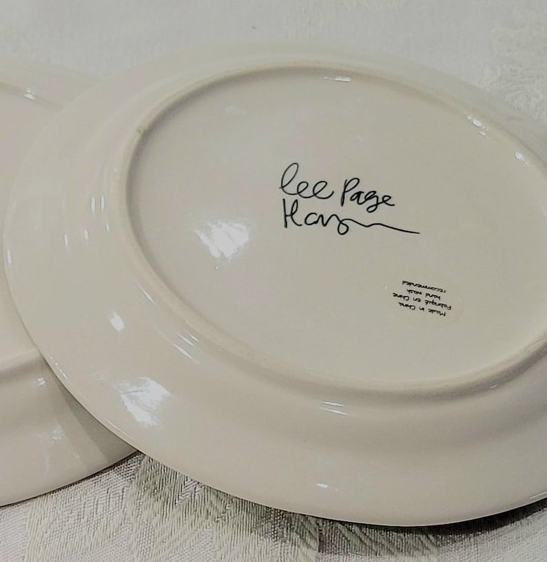 May include: White oval ceramic plate with black handwritten text "Lee Page Home" on the bottom. The plate has a black printed label with the text "Microwave, Oven, Dishwasher Safe" in a circle.