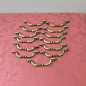 May include: A set of 12 antique gold cabinet door pulls. The pulls are made of metal and have a simple, elegant design.