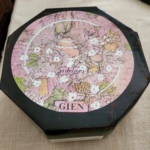 May include: A black octagonal box with a pink and white floral design. The box has a white label with the text "Gien" and "Les Delices" in a script font.