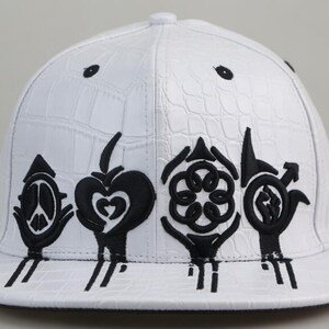 May include: White baseball cap with a crocodile-embossed leather design. The cap features black embroidered symbols, including a peace sign, a heart, a flower, and a fist.