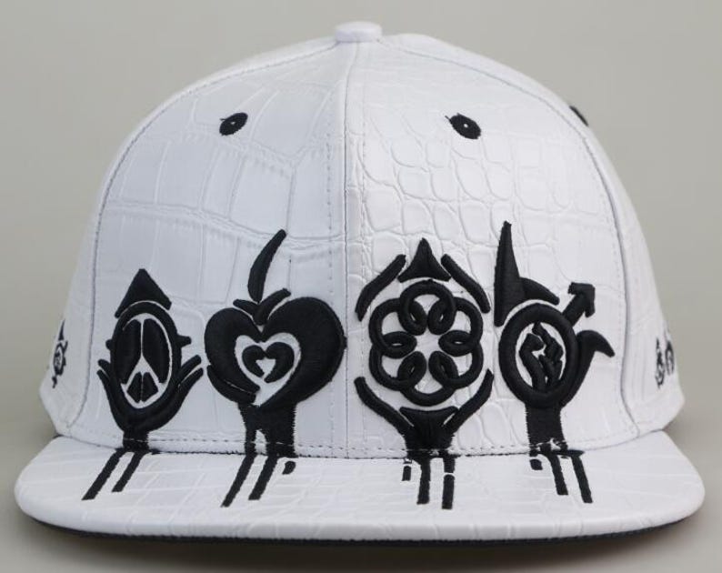 May include: White baseball cap with a crocodile-embossed leather design. The cap features black embroidered symbols, including a peace sign, a heart, a flower, and a fist.