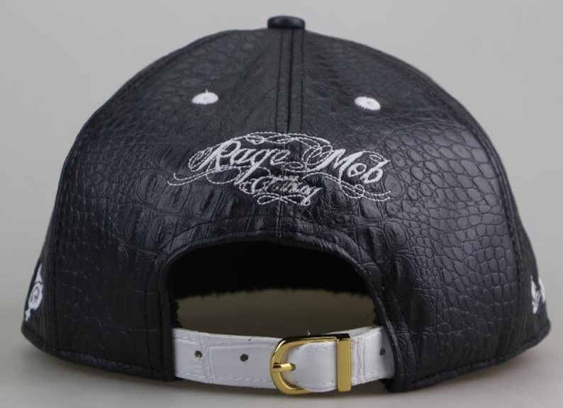 Puede incluir: Gorra de b&eacute;isbol de cuero negro con una correa de cuero blanco y un logotipo bordado en blanco que dice "Rage Mob Clothing".