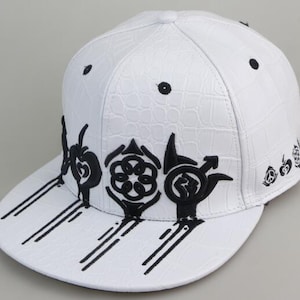 May include: White leather baseball cap with black embroidered designs. The cap has a crocodile-embossed texture and a flat brim.