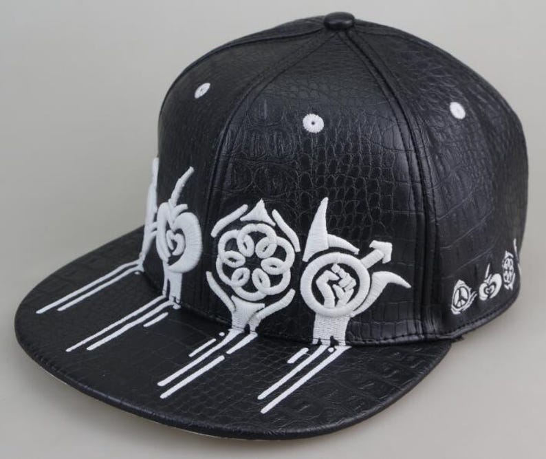 Puede incluir: Gorra de b&eacute;isbol de cuero negro con dise&ntilde;os bordados en blanco. Los dise&ntilde;os incluyen una flor estilizada, un pu&ntilde;o y otras formas abstractas.