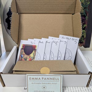 May include: An open cardboard box containing embroidery supplies. Inside are small packets labeled "Parls", "Beads", "Thread", and "Spiral". A business card for Emma Pannell, Multimedia Embroidery Artist, is visible.