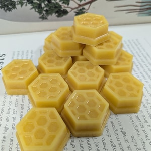 May include: A pile of yellow, hexagonal beeswax melts, each featuring a honeycomb design. The melts are arranged on a book with text about mangroves and tropical ecosystems. The image evokes a natural, eco-conscious theme.