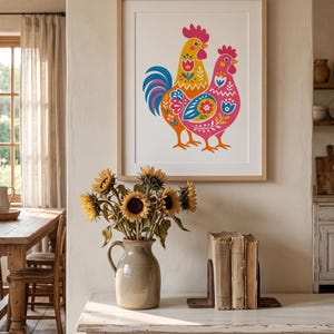 Puede incluir: Una lámina de arte enmarcada que muestra una ilustración colorida de dos gallos uno al lado del otro. Los gallos están decorados con patrones florales y geométricos en tonos amarillo, rosa, naranja, azul y rojo sobre fondo blanco.