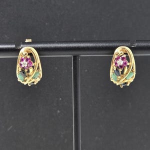 May include: A pair of gold earrings featuring a floral design with a central pink gemstone surrounded by small clear stones, accented by marquise-cut dark blue and green gemstones set within a curved gold frame that forms a teardrop shape.