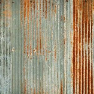 Pode incluir: Close-up de uma chapa metálica ondulada desgastada. O metal tem um padrão de nervuras verticais com uma mistura de tons azul-cinza e laranja enferrujado. A superfície mostra sinais de idade e exposição aos elementos, com áreas de ferrugem e descoloração.