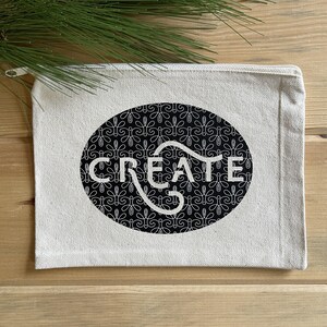 May include: A white canvas zippered pouch with a black oval design. The oval has a white pattern and the word "CREATE" in white lettering.