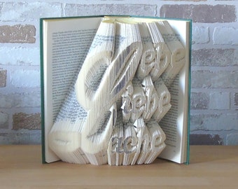 May include: A book with the German words "Liebe" (love) and "Heime" (home) folded into a 3D design. The book is open and the pages are folded to create the words.