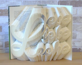 May include: A white book with the word "Love" folded into the pages. The book is open and the pages are folded to create a 3D effect.