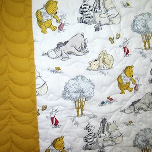 May include: A white fabric with a yellow border features a repeating pattern of Winnie the Pooh and his friends. The characters are depicted in various poses, including standing, sitting, and lying down. The fabric is quilted with a subtle pattern.