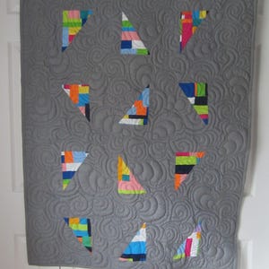 May include: A gray quilt with a swirl pattern and colorful geometric triangles. The triangles are made of different fabrics with various colors and patterns.