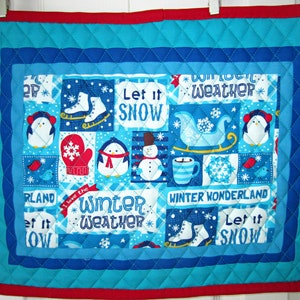 May include: A blue quilted fabric wall hanging with a winter theme. It features penguins, snowflakes, a snowman, a sled, ice skates, and the text "Let it snow", "Winter weather", and "Winter Wonderland".