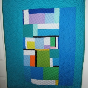 May include: A turquoise blue quilt with a geometric pattern of colorful squares and rectangles. The quilt is quilted with a swirling pattern.