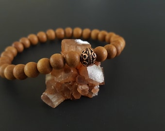May include: A brown wooden beaded bracelet with a copper-colored metal bead. The bracelet is resting on a cluster of light brown crystals.