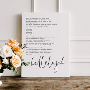 May include: A white canvas print with black text featuring the lyrics to the song "Hallelujah" by Leonard Cohen. The lyrics are printed in a simple, modern font. The print is framed with a white border.