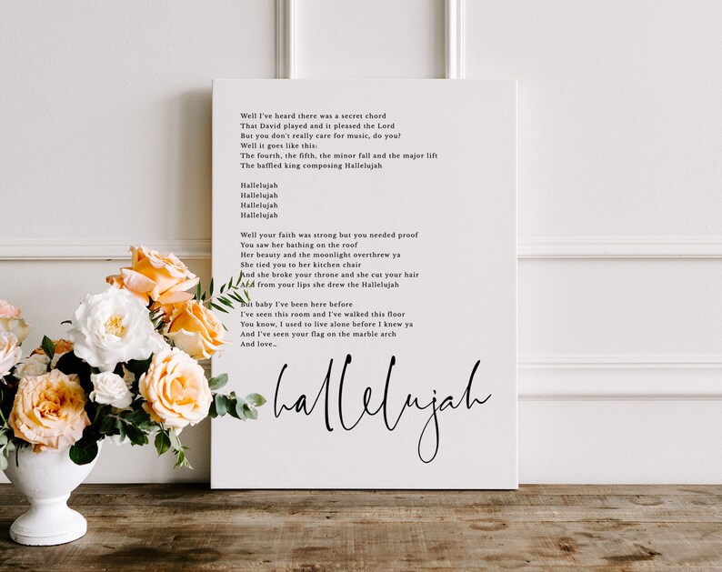 May include: A white canvas print with black text featuring the lyrics to the song "Hallelujah" by Leonard Cohen. The lyrics are printed in a simple, modern font. The print is framed with a white border.