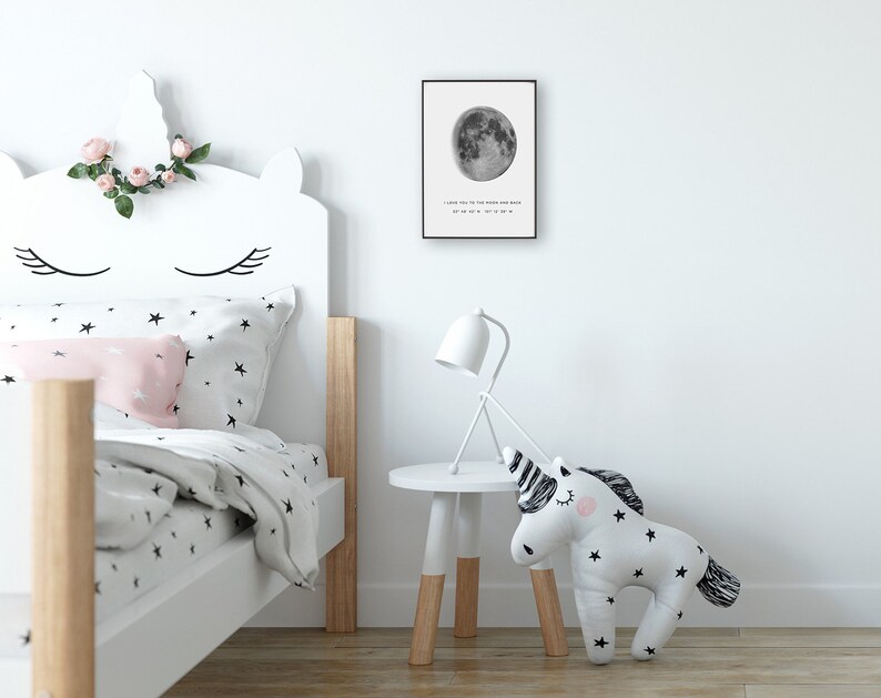 Puede incluir: Una impresi&oacute;n en blanco y negro de una luna llena con el texto "I love you to the moon and back" y una serie de n&uacute;meros debajo. La impresi&oacute;n est&aacute; enmarcada y colgada en una pared blanca sobre una cama blanca con una cabecera de unicornio.