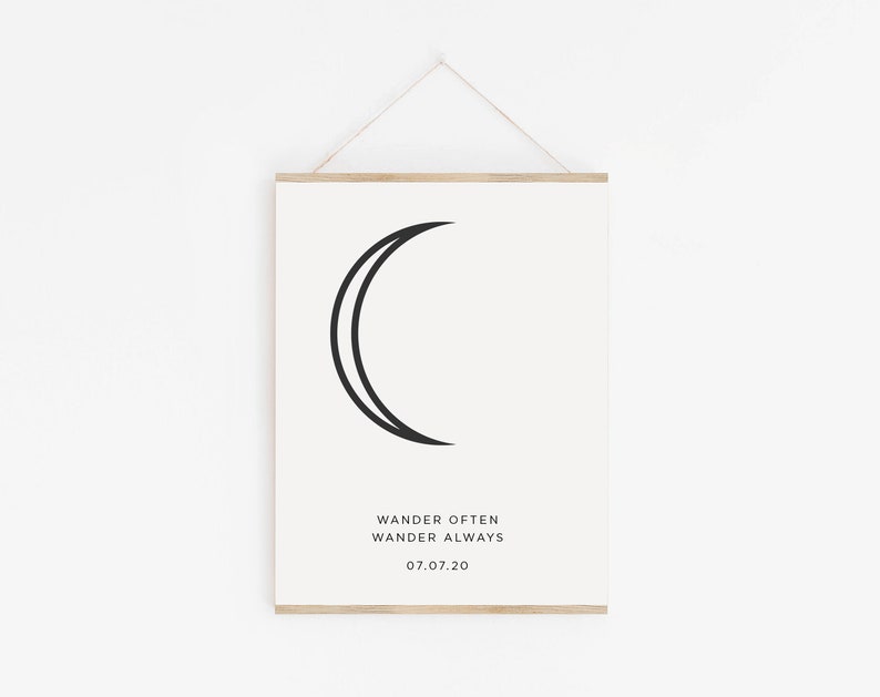 May include: A black and white print with a crescent moon design and the text "Wander Often Wander Always 07.07.20". The print is framed with a light wood frame.