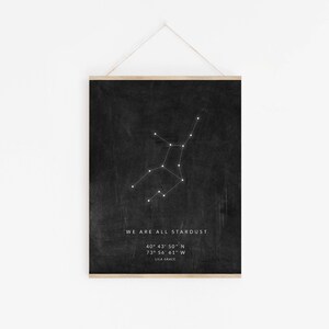May include: Black and white print with a constellation of stars on a black background. The text "WE ARE ALL STARDUST" is at the bottom of the print, along with the coordinates "40&deg; 43' 50" N 73&deg; 56' 61" W" and the name "LILA GRACE".