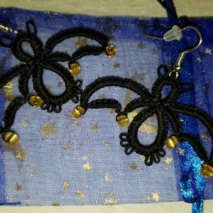 Pode incluir: Um par de brincos de croch&ecirc; preto com contas douradas penduradas em uma bolsa de malha azul e dourada.