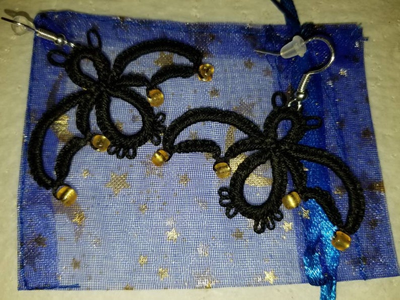 Pode incluir: Um par de brincos de croch&ecirc; preto com contas douradas penduradas em uma bolsa de malha azul e dourada.