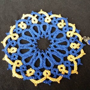 K&ouml;nnte beinhalten: Eine geh&auml;kelte Deckchen in Blau und Gold mit einem kleinen blauen Schmuckanh&auml;nger.