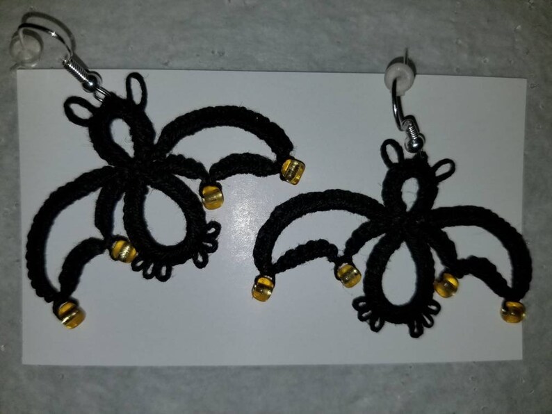 Pode incluir: Um par de brincos de morcego de croch&ecirc; preto com contas douradas. Os brincos est&atilde;o pendurados em ganchos prateados.
