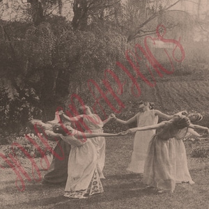 May include: Sepia-toned photograph of a group of women in flowing dresses dancing in a circle outdoors. They are holding hands, with their arms outstretched. The background includes trees, grass, and a field.