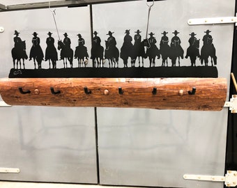 May include: A rustic wooden coat rack with metal hooks and a metal silhouette of cowboys riding horses. The silhouette is black and the wood is brown.