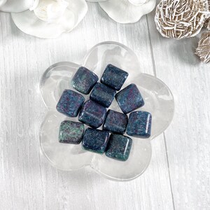 May include: A collection of ten tumbled blue kyanite stones with red and green inclusions, displayed in a clear flower-shaped dish.