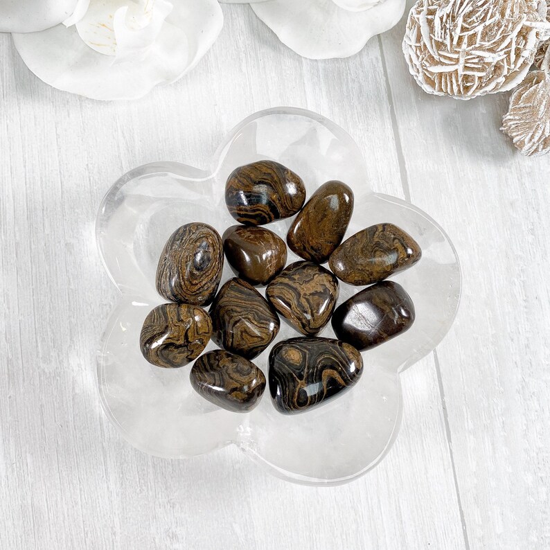 May include: A collection of brown and black tiger iron tumbled stones in a clear flower-shaped dish.