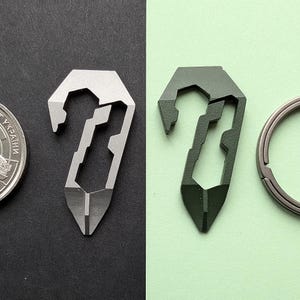 May include: A silver and a dark green multi-tool keychain. The multi-tools have a hook, a flathead screwdriver, and a pointed end. A silver keyring is also visible.