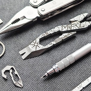 以下が含まれることがあります： マルチツール、コンパスをテーマにしたツール、ペン、小さな栓抜きなど、銀色のツールのコレクションです。「Victorinox」のブランドが刻印されています。ツールは、質感のある灰色の表面に配置されています。