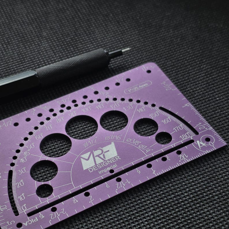 May include: A purple metal drafting template with a protractor, circular cutouts, and imperial measurement markings. The tool features the text MRF DESIGNER imperial and 1 inch equals 25.4 mm. A black mechanical pencil rests above the tool.