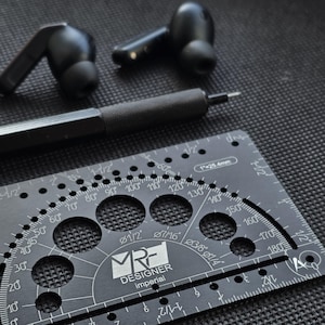 May include: A pair of black wireless earbuds, a black mechanical pencil, and a black metal drafting template tool featuring imperial measurements, degree markings, and circular cutouts with the text MRF DESIGNER imperial.