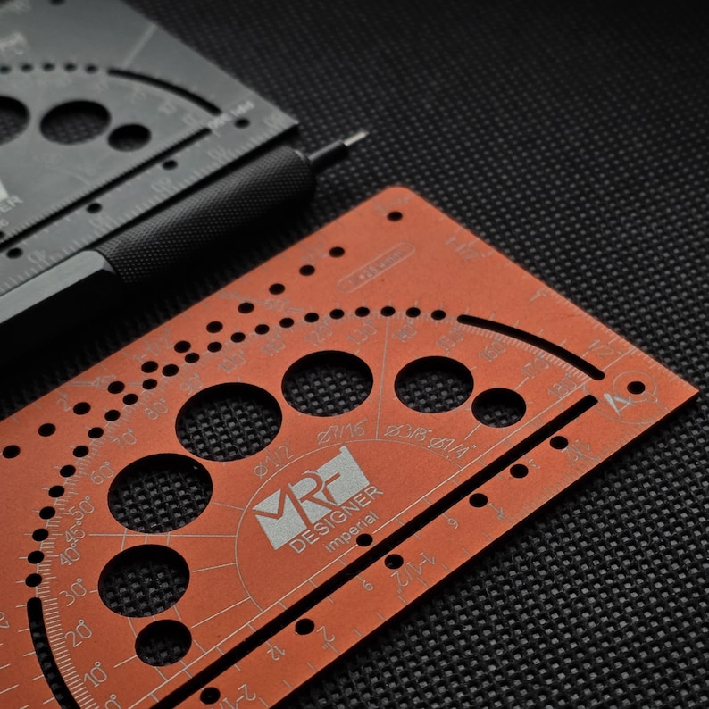 May include: A copper-colored metal drafting template featuring circular cutouts, angle markings, and the text MRF DESIGNER imperial. A black metal mechanical pencil with a textured grip rests alongside a second black drafting template.